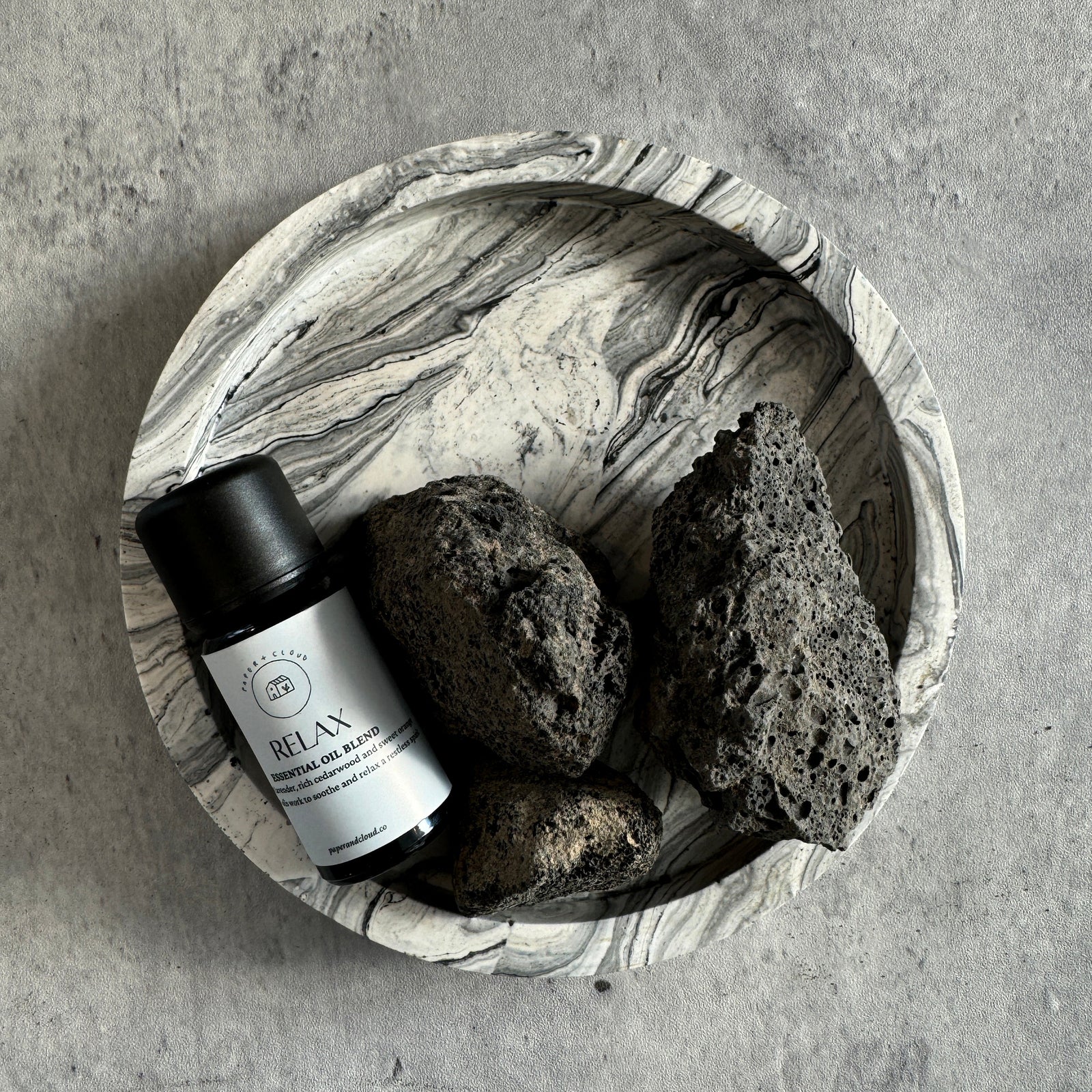handmade Bowl with a bottle labeled 'Relax' and two black stones on a gray surface
