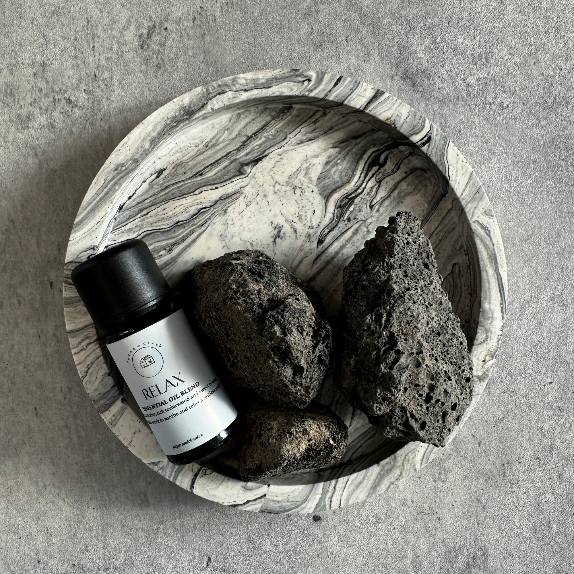handmade Bowl with a bottle labeled 'Relax' and two black stones on a gray surface