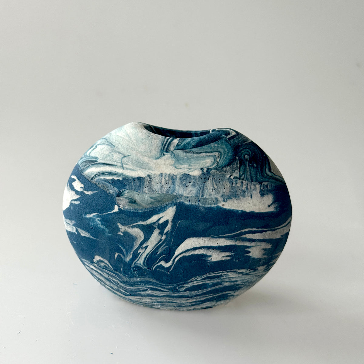 A small round ceramic vase with a deep, slightly tapered opening, featuring a marbled swirl pattern of deep navy blue and white.