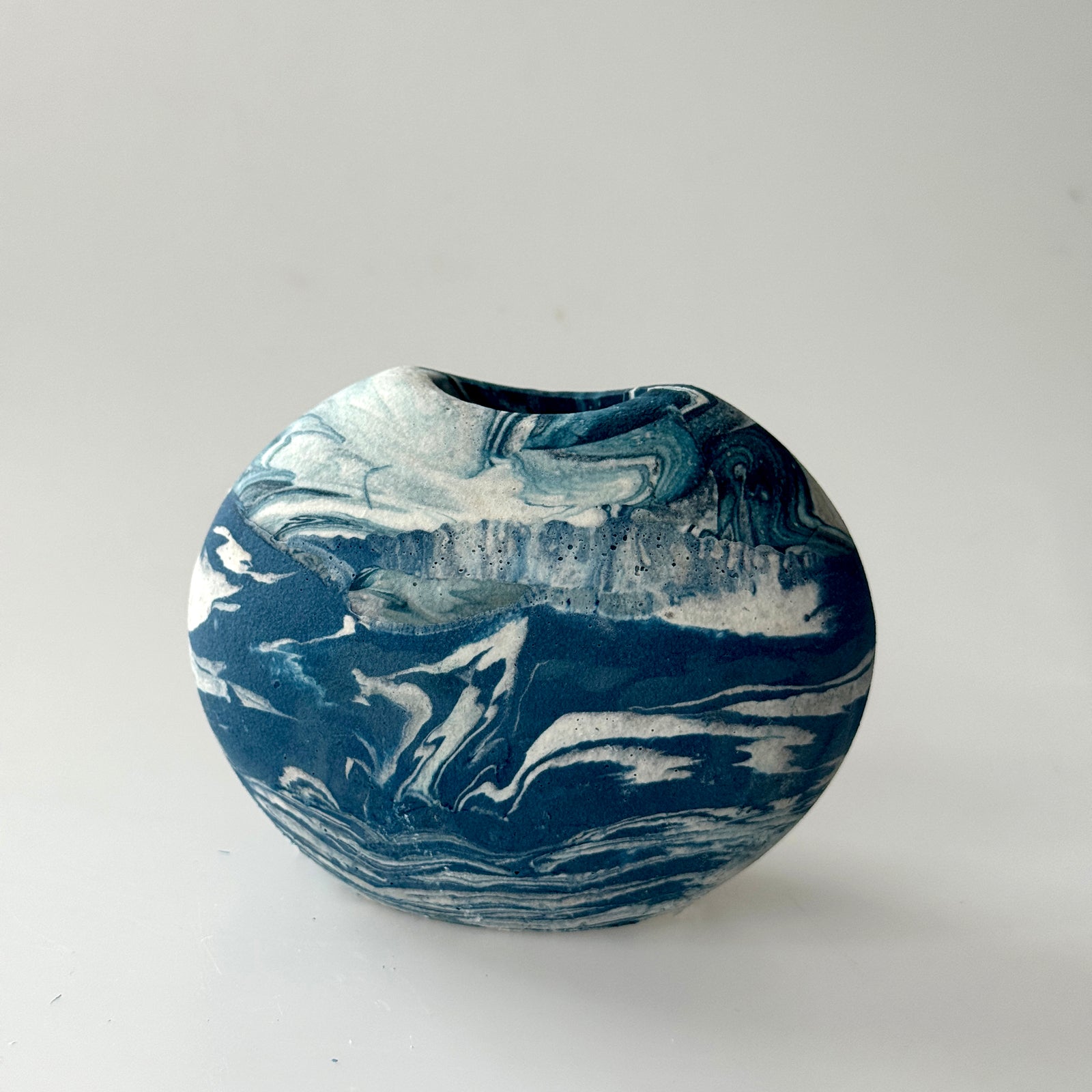 A small round ceramic vase with a deep, slightly tapered opening, featuring a marbled swirl pattern of deep navy blue and white.